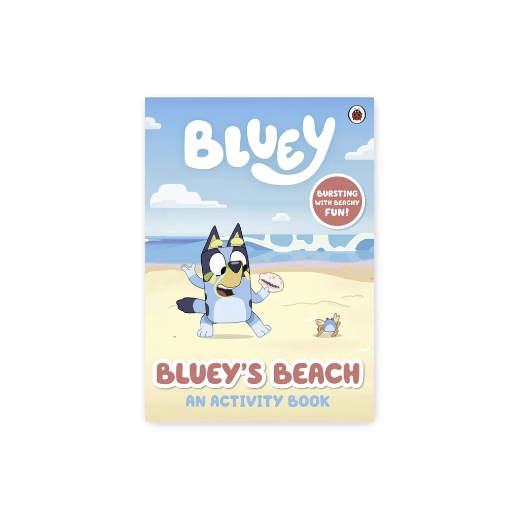Okładka książki „Bluey’s Beach” przedstawiająca Bluey siedzącą na plaży z pączkiem i krabem, z napisem „Bursting with beachy fun!”